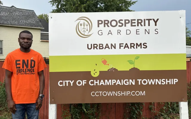 The author next to the sign for the City of Champaign Township’s Prosperity Gardens project in downtown Champaign.