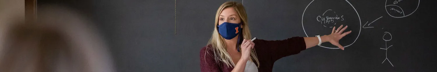 Instructor teaching class in front of blackboard.